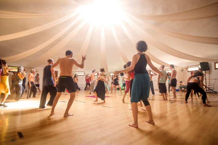 Una sala luminosa con gente bailando ecstatic dance.